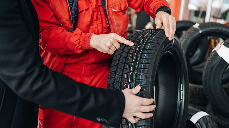 Young handsome customer after fueling his car on gas station looking for some good new winter tires. He is talking with salesman and asking him for advice. Credit: mladenbalinovac iStock.com